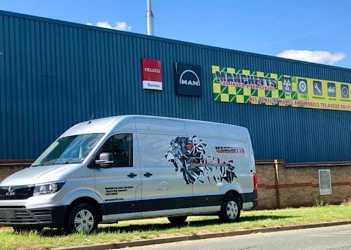 White delivery van parked by a blue industrial building with Manchetts signs and a colorful mural.