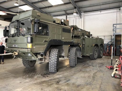 Military-green 6x6 armored vehicle parked inside a workshop garage