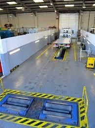 Industrial workshop with a large blue machine pit marked by yellow caution stripes inside a warehouse.