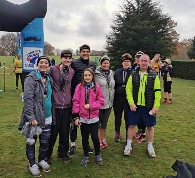 Group of runners posing outdoors on grass, wearing athletic jackets and a bright yellow vest.