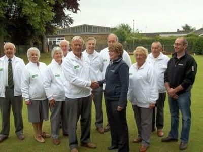 Group posing outdoors, shaking hands in front of a building, many wearing white jackets