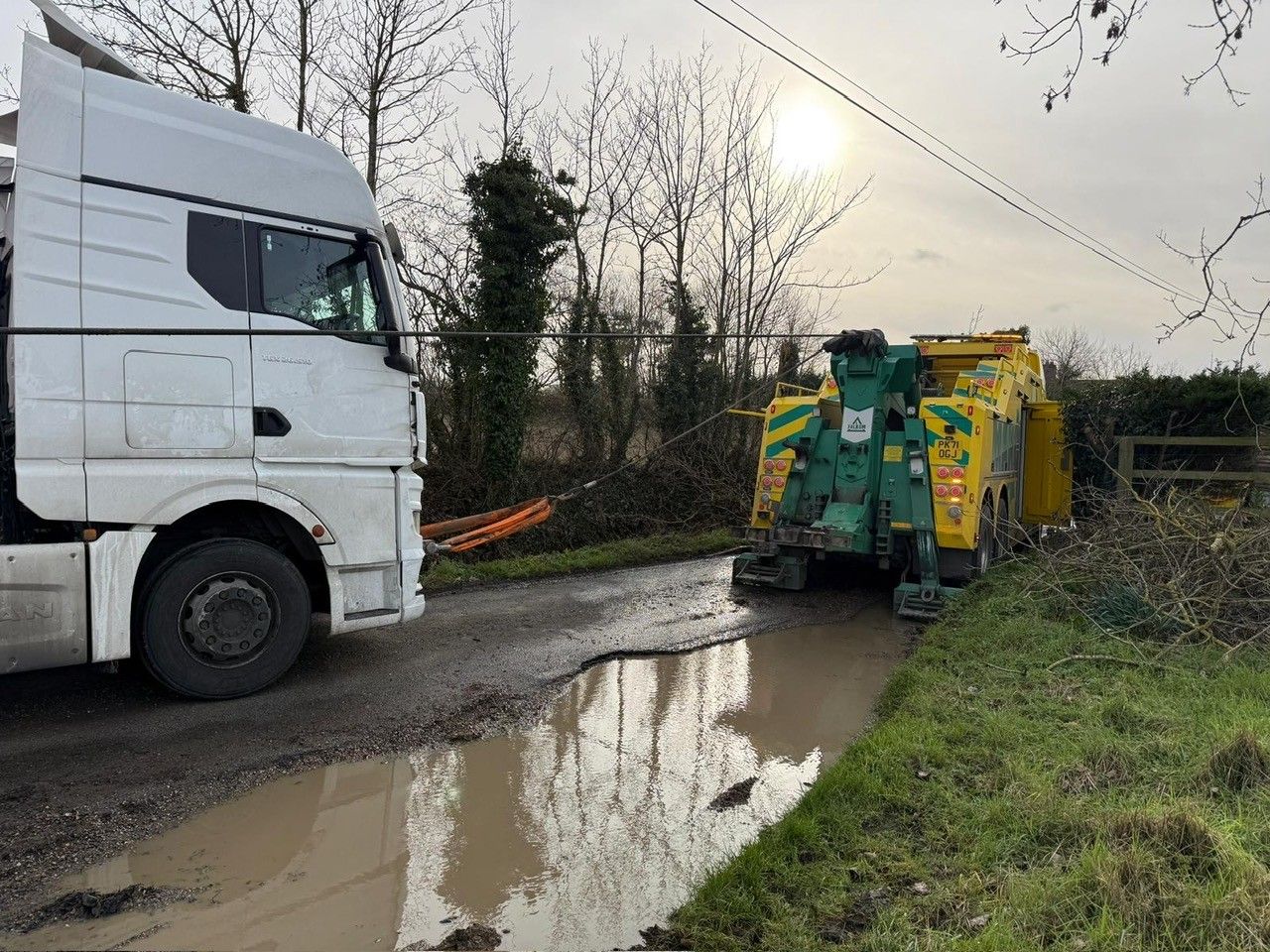 White truck and two waste bins on a muddy country road beside a puddle, under a cloudy sky