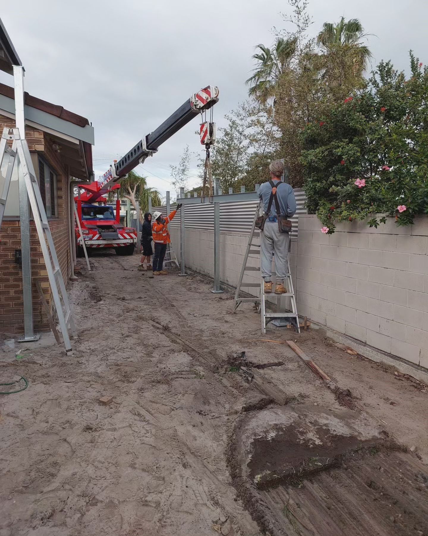 A Man Is Standing On A Ladder Next To A Crane — Pottsville Carpentry and Home Maintenance In Pottsville, NSW