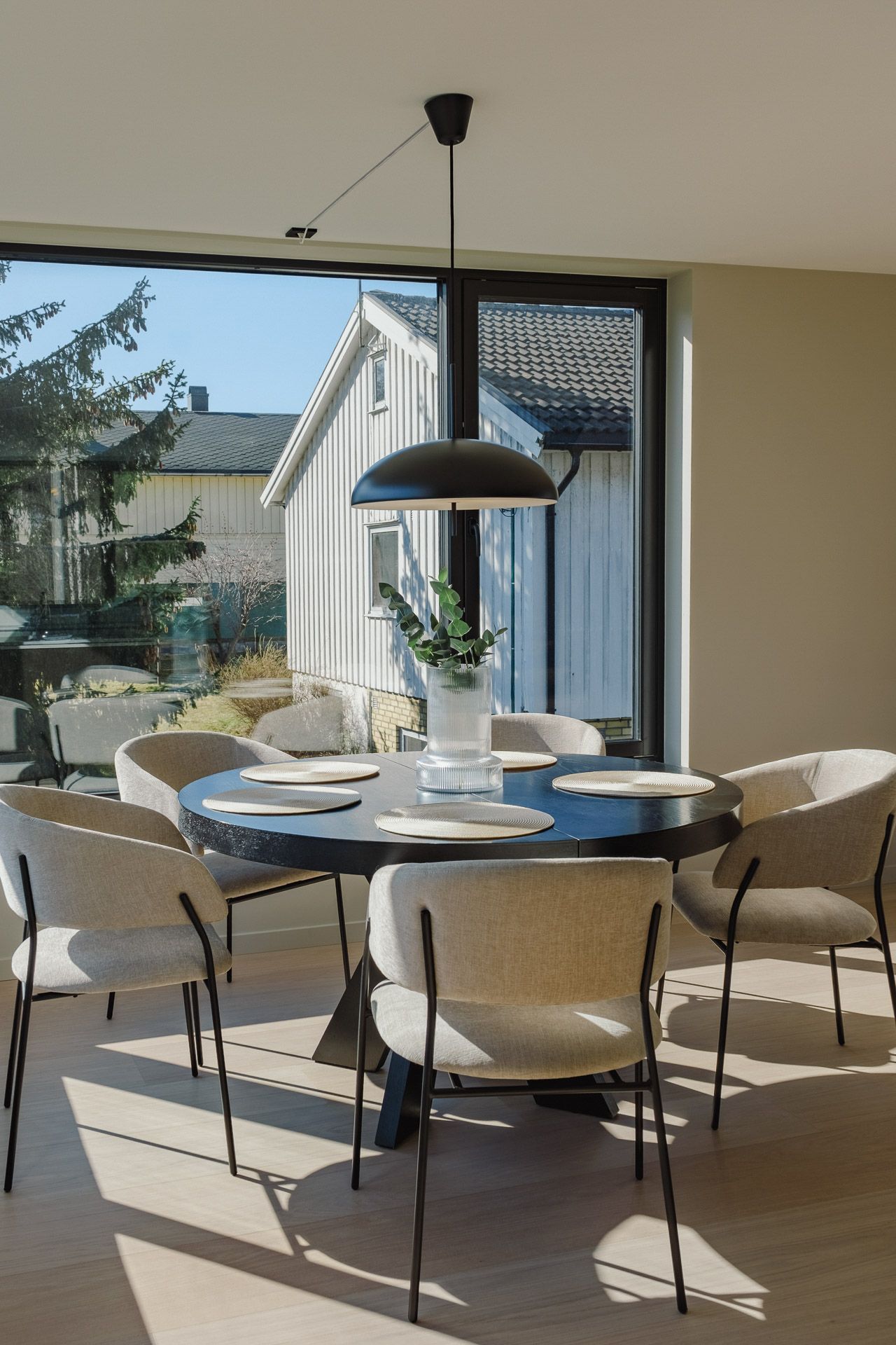 Moderne spisestue med rundt bord, hvite stoler og store skyvedører i glass som åpner ut mot en terrasse.