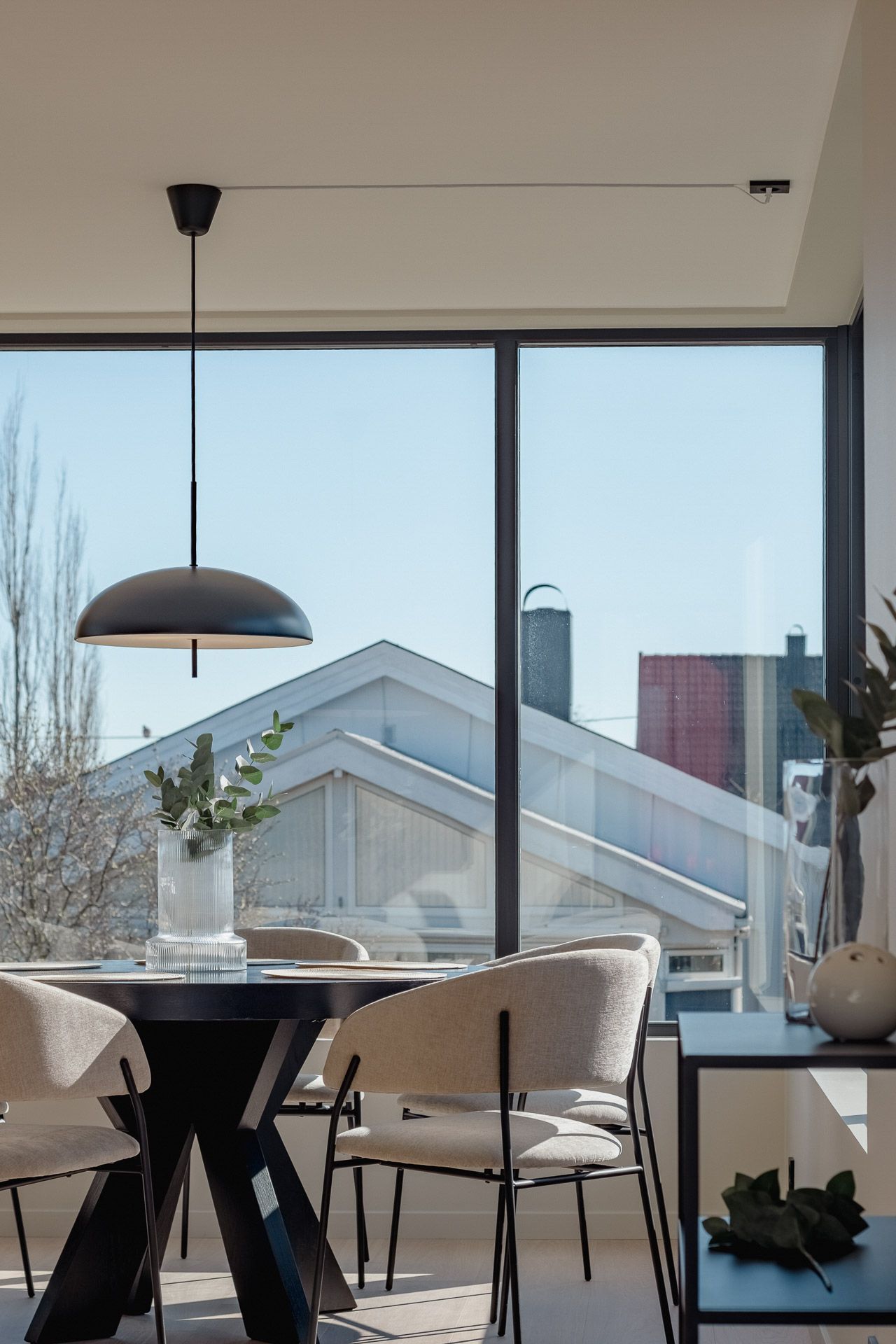 Moderne spisestue med hengelampe, rundt bord, stoler og utsikt over byen gjennom store vinduer