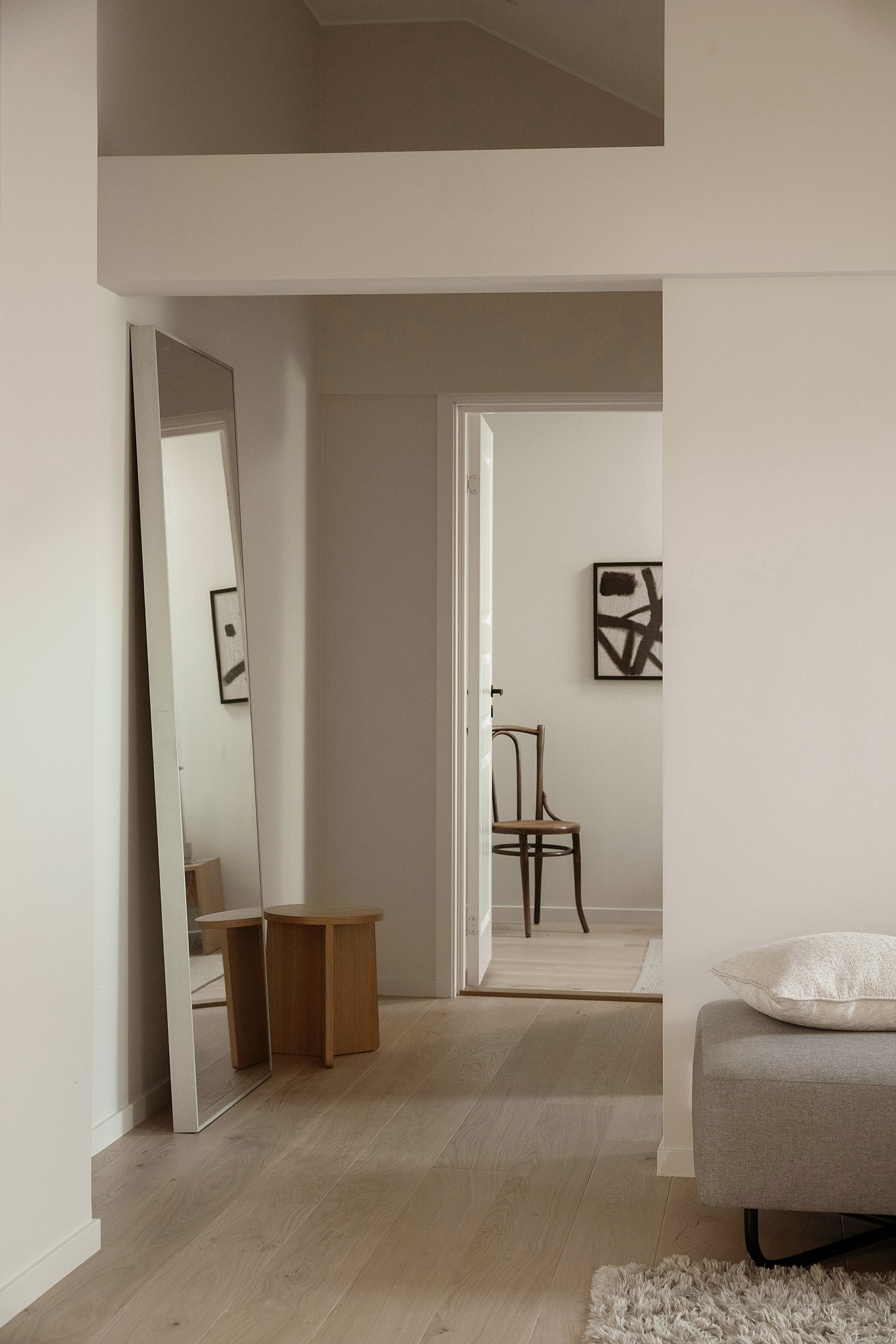 Minimalistisk gang med et stort speil, trekrakk og delvis sofa i beige interiør.