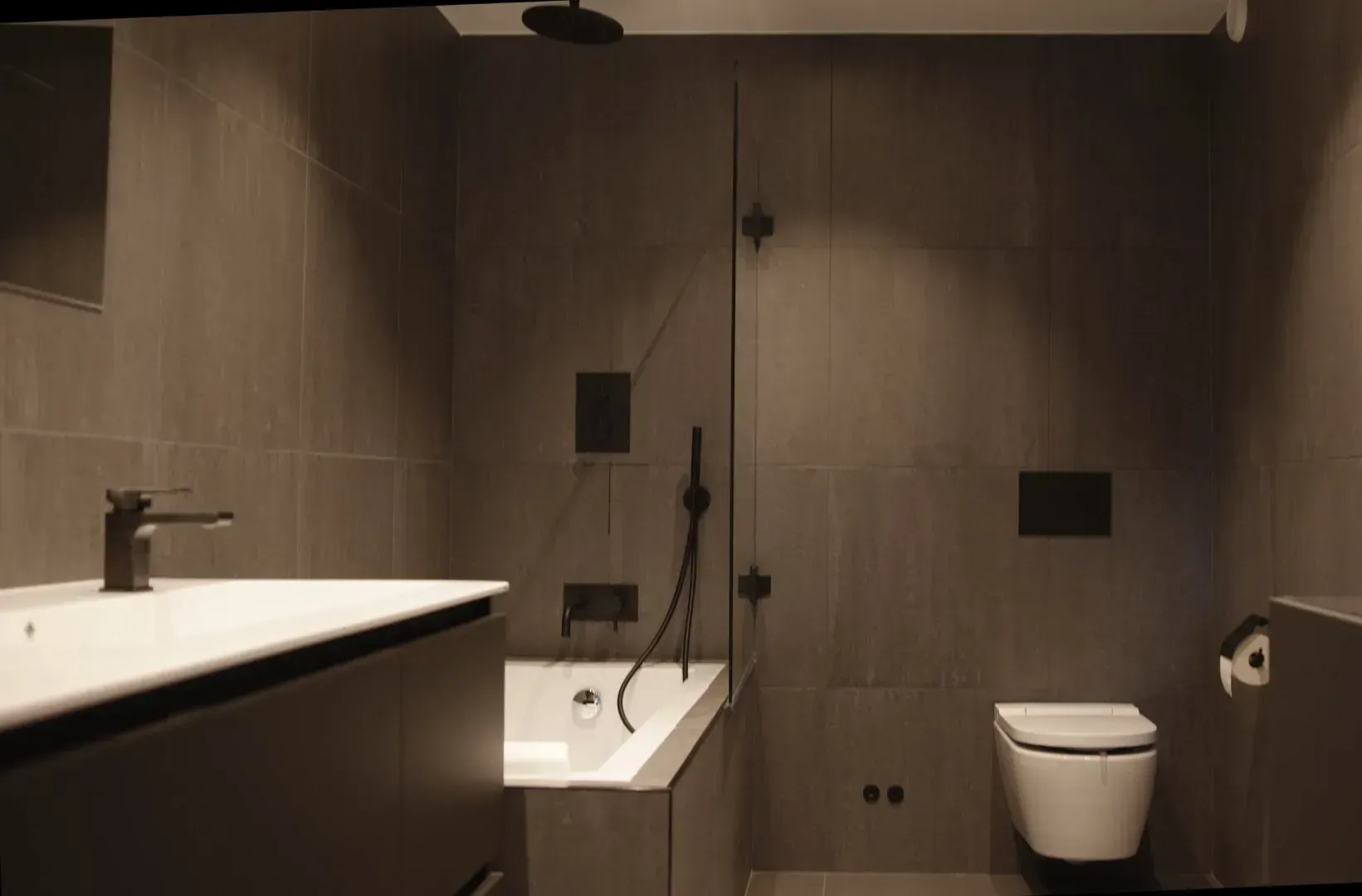 Moderne minimalistisk bad med hvitt badekar, vask, toalett og mørke flislagte vegger