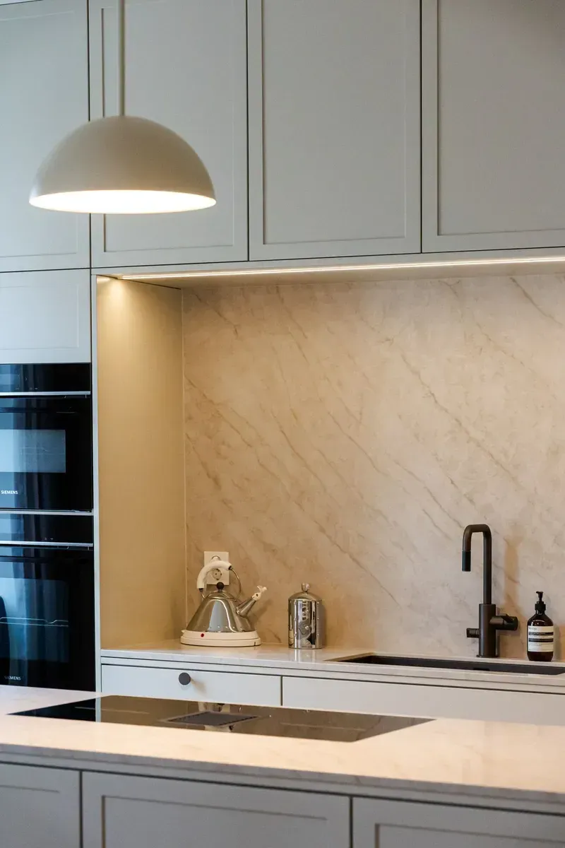 Moderne kjøkkenvask med beige skap, marmor bakplate og en hengende pendellampe
