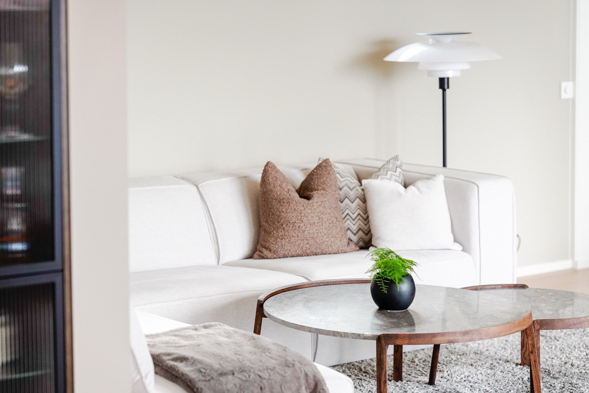Lys stue med hvit sofa, brune puter, salongbord i glass og gulvlampe