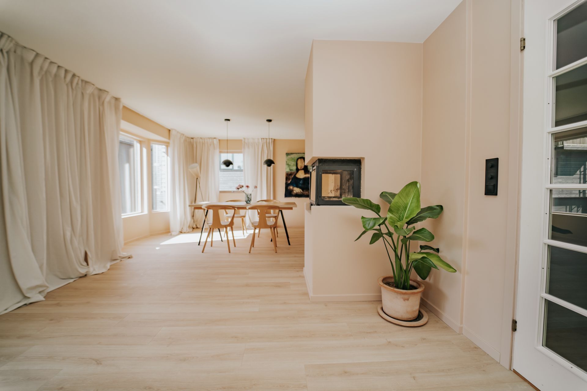Lys og moderne stue med oppgradert peis i minimalistisk design, lyse tregulv og store vinduer som sl