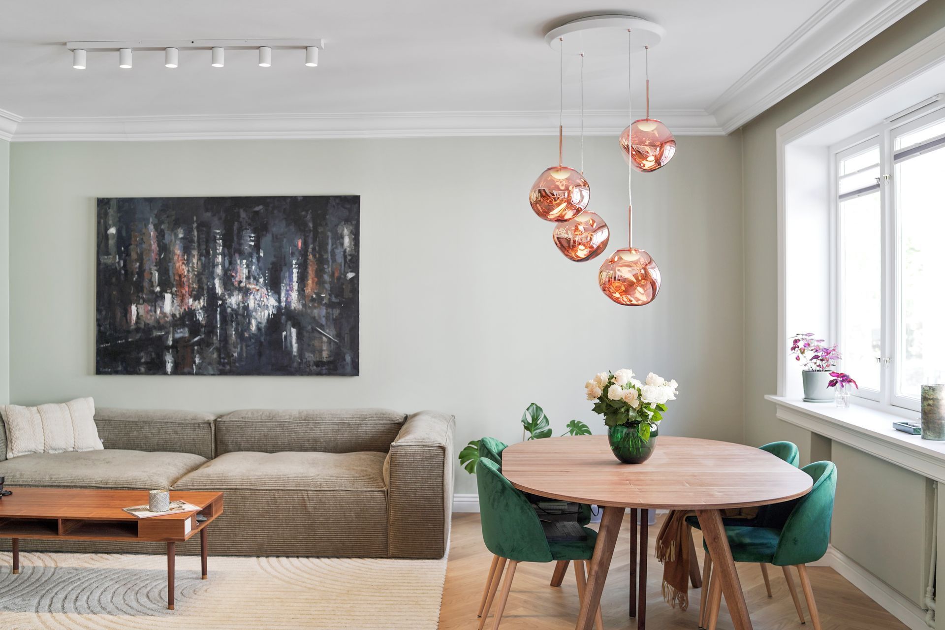 Moderne stue-spisestue med grå sofa, abstrakt veggkunst, rundt bord, grønne stoler og kobberhengelamper