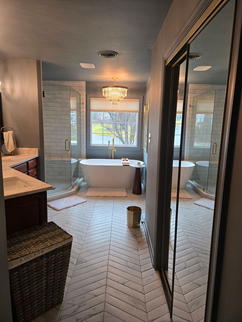 Modern bathroom with freestanding tub, glass shower, and herringbone tile floor near a window.