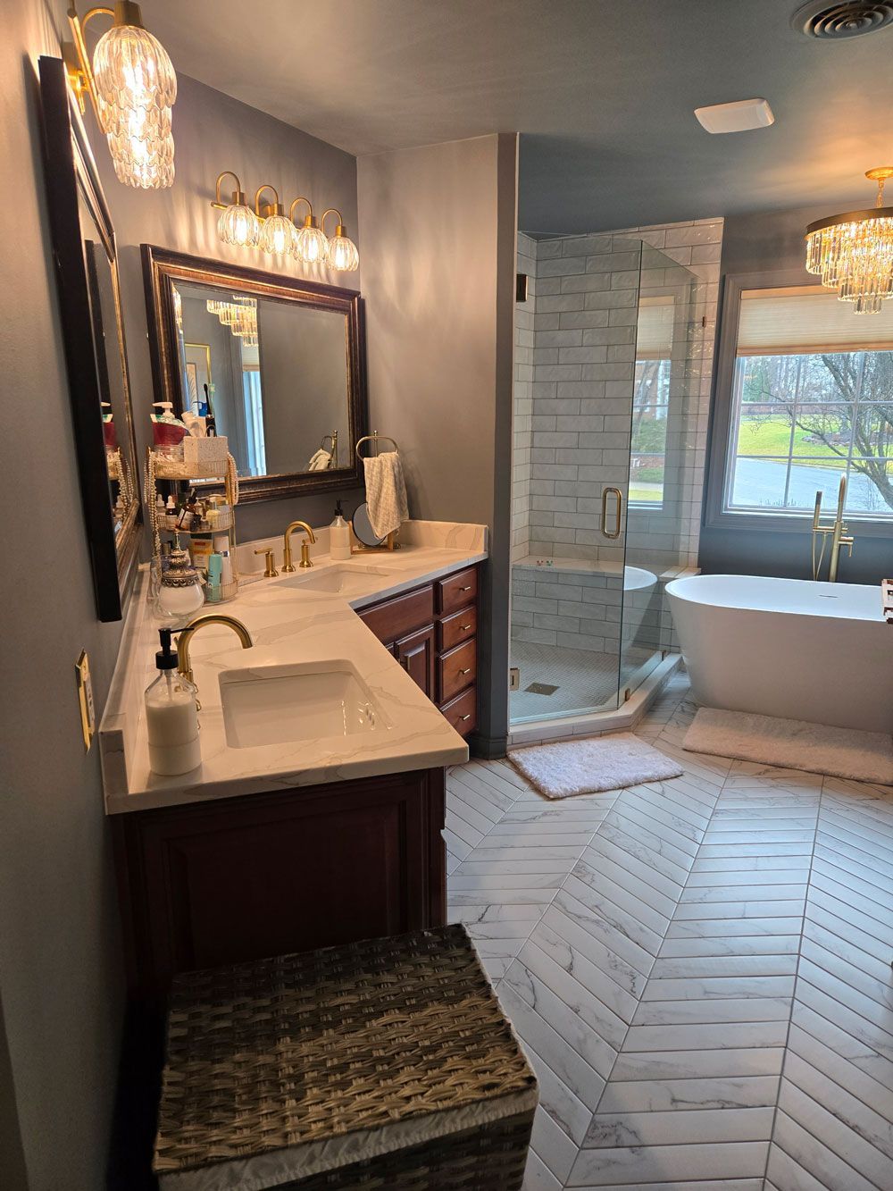 Bathroom vanity with large mirror, dark wood cabinets, and a freestanding tub by a window in a bright tiled room