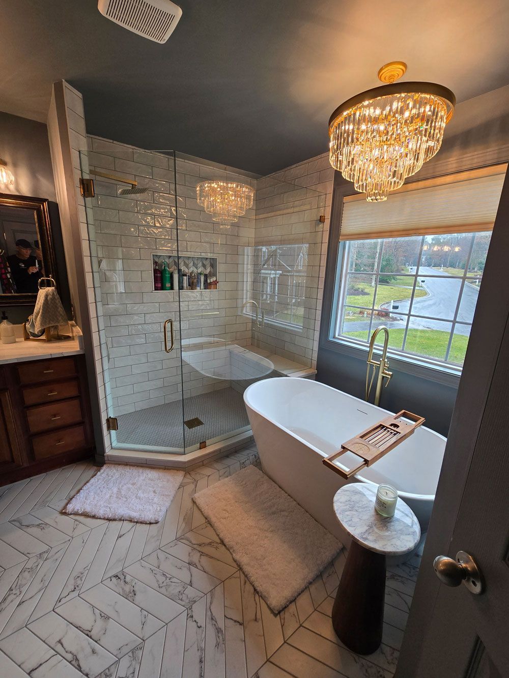 Elegant bathroom with glass shower, freestanding tub, chandelier, and herringbone tile floor