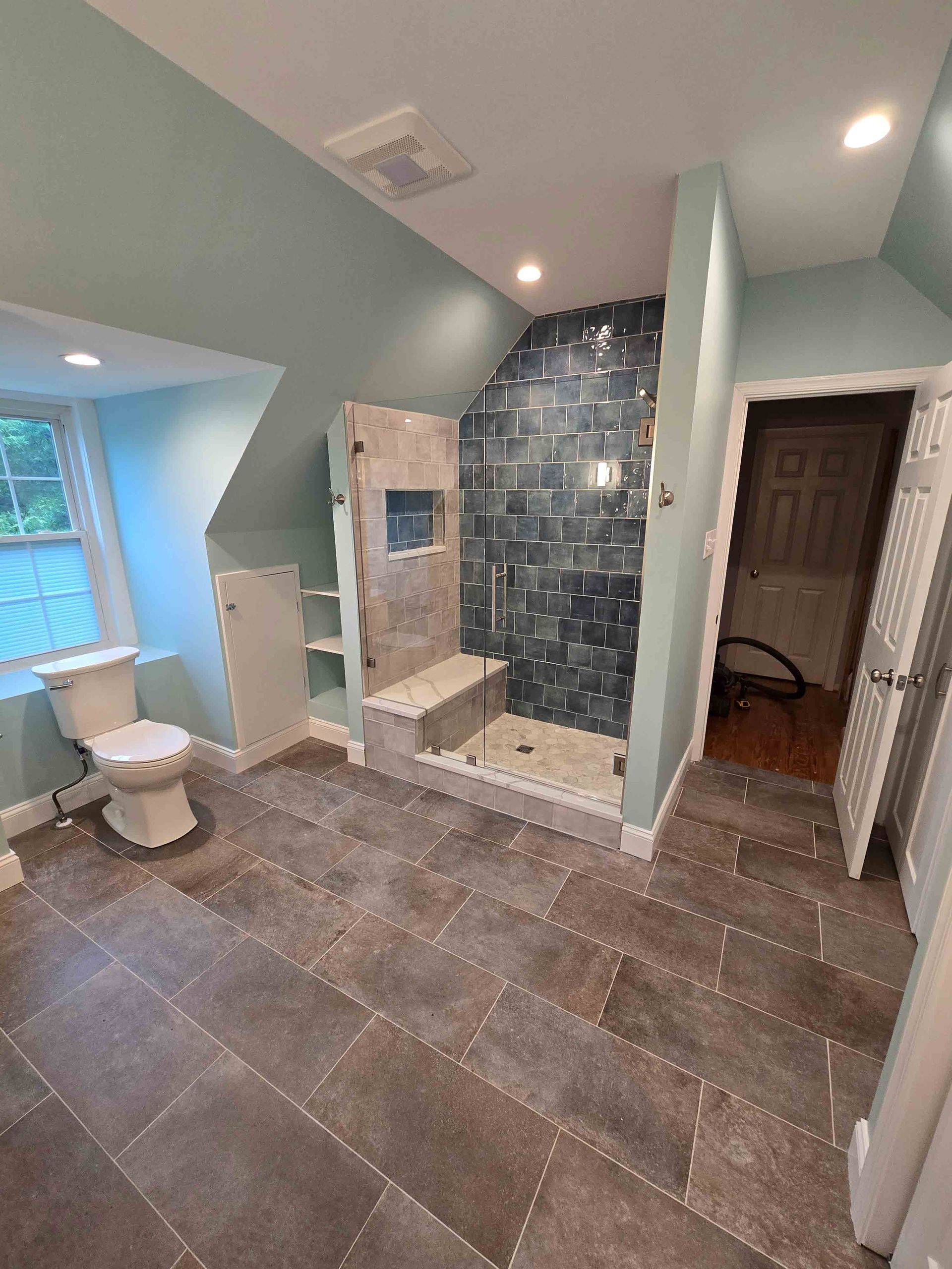 A bathroom with a toilet , shower , and window.