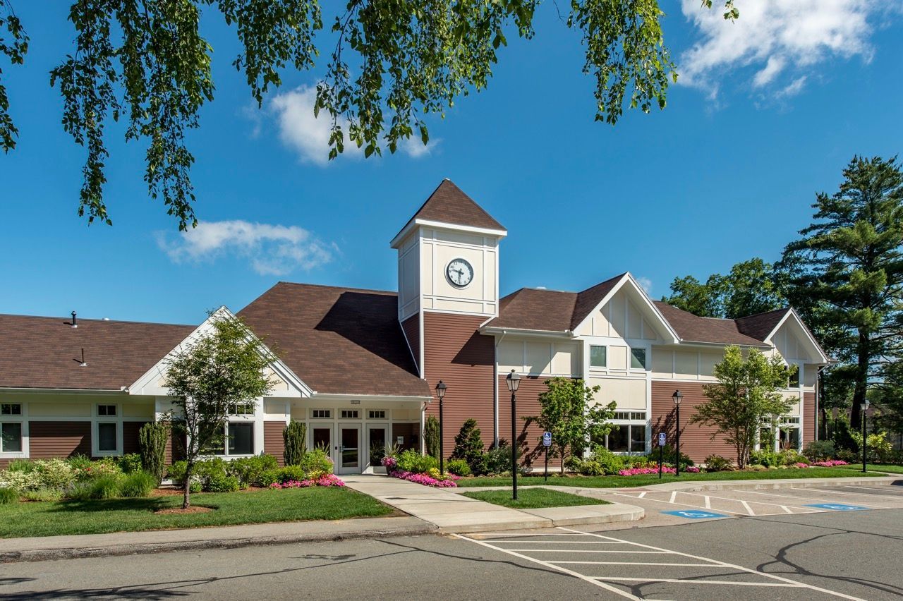 Exterior view of a multifamily community building with a clock tower, entryway, and landscaped front lawn.