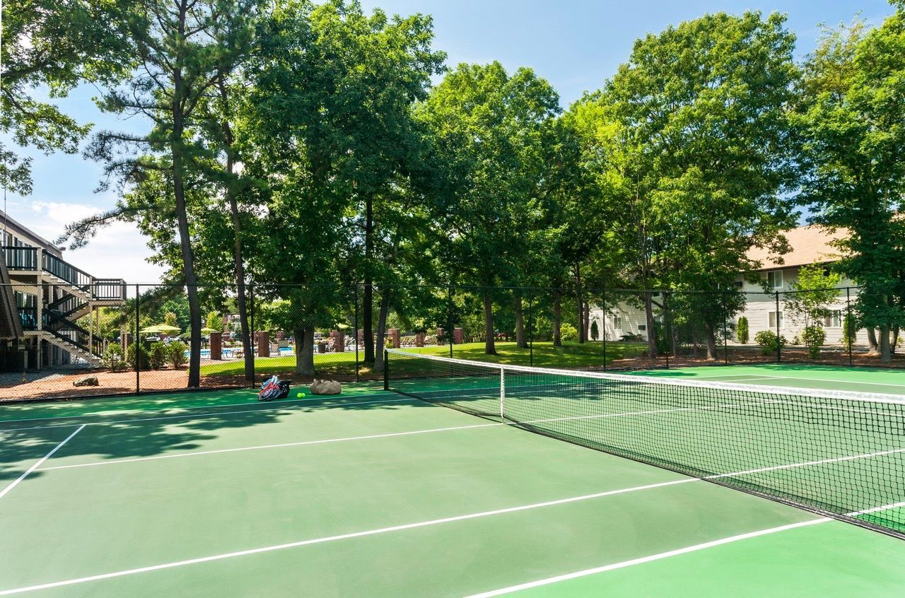 Outdoor tennis court with net, surrounded by trees and apartment buildings.