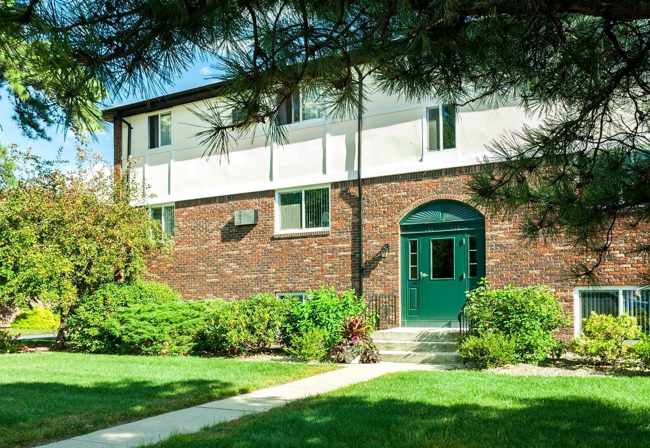 Exterior view of a brick multifamily building entrance with a green door and landscaped lawn.