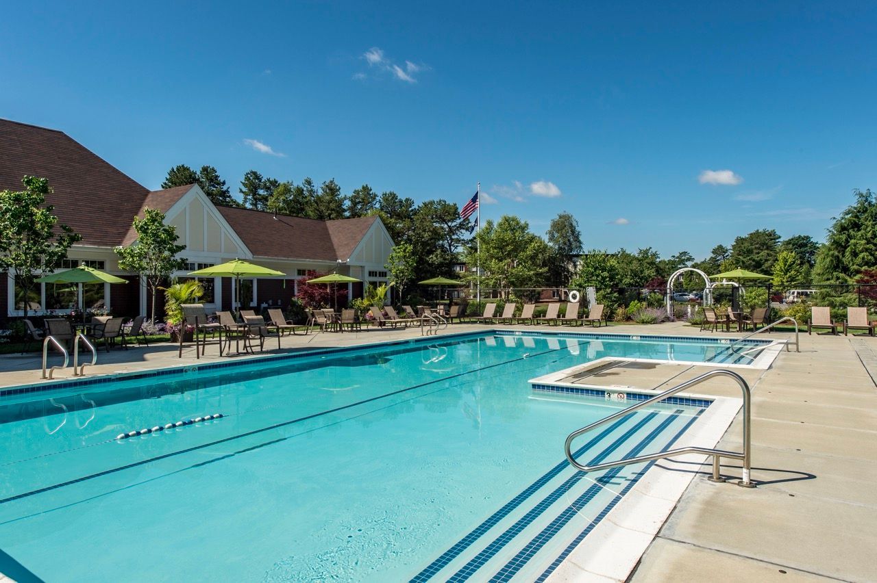 Outdoor community pool with lounge chairs and green umbrellas near a clubhouse.
