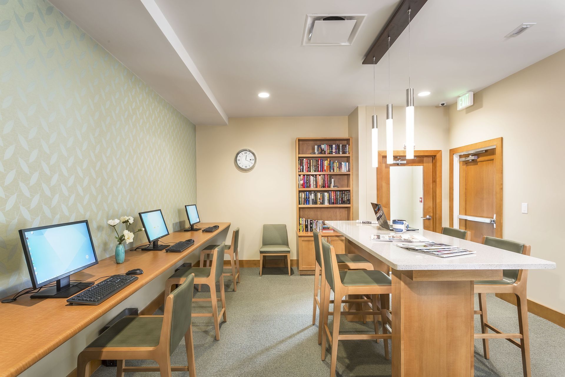 Computer lab with wooden desks, desktop monitors, chairs, and a white table in a bright room