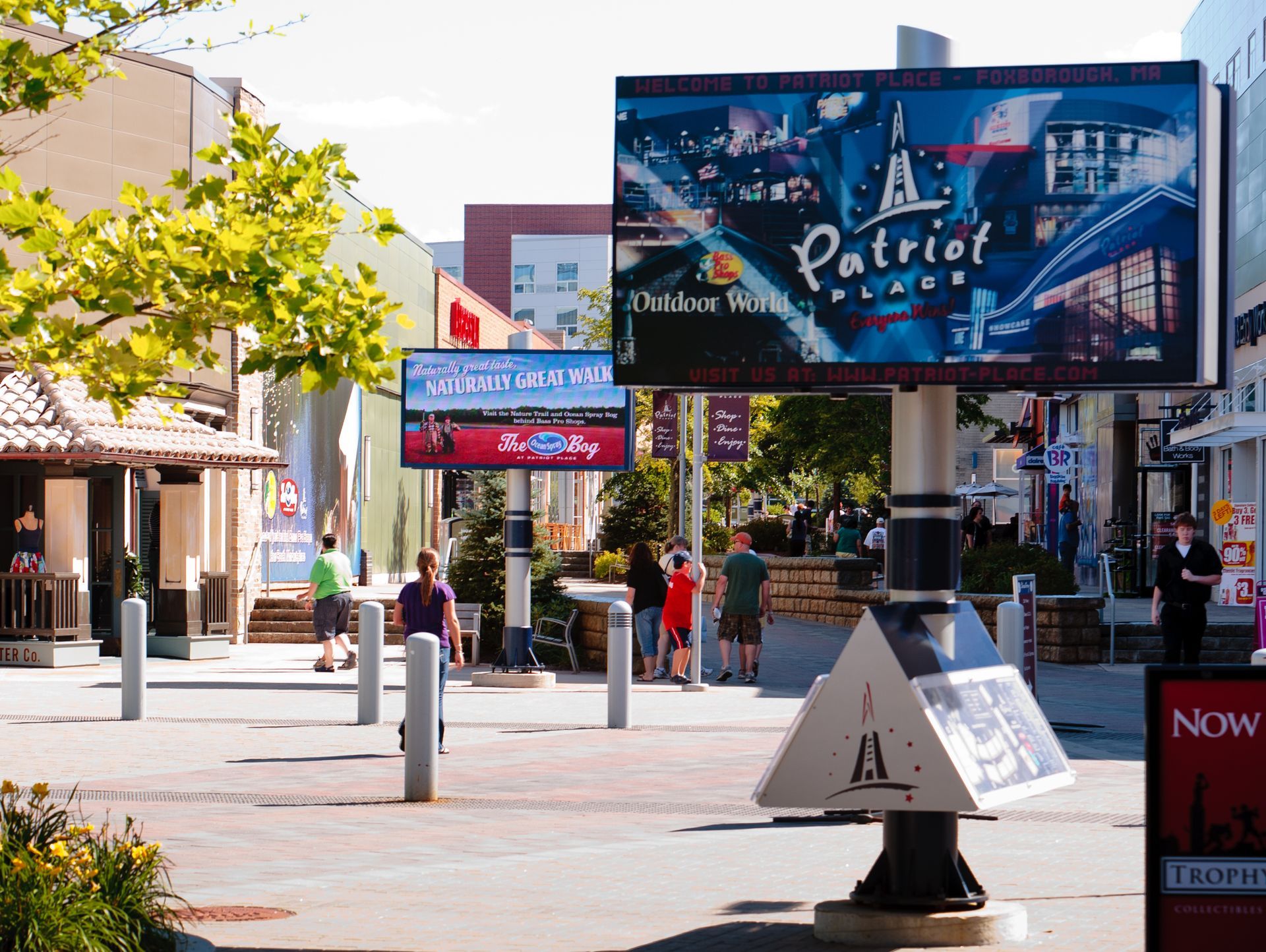 Outdoor shopping street with colorful signs, trees, and pedestrians on a sunny day