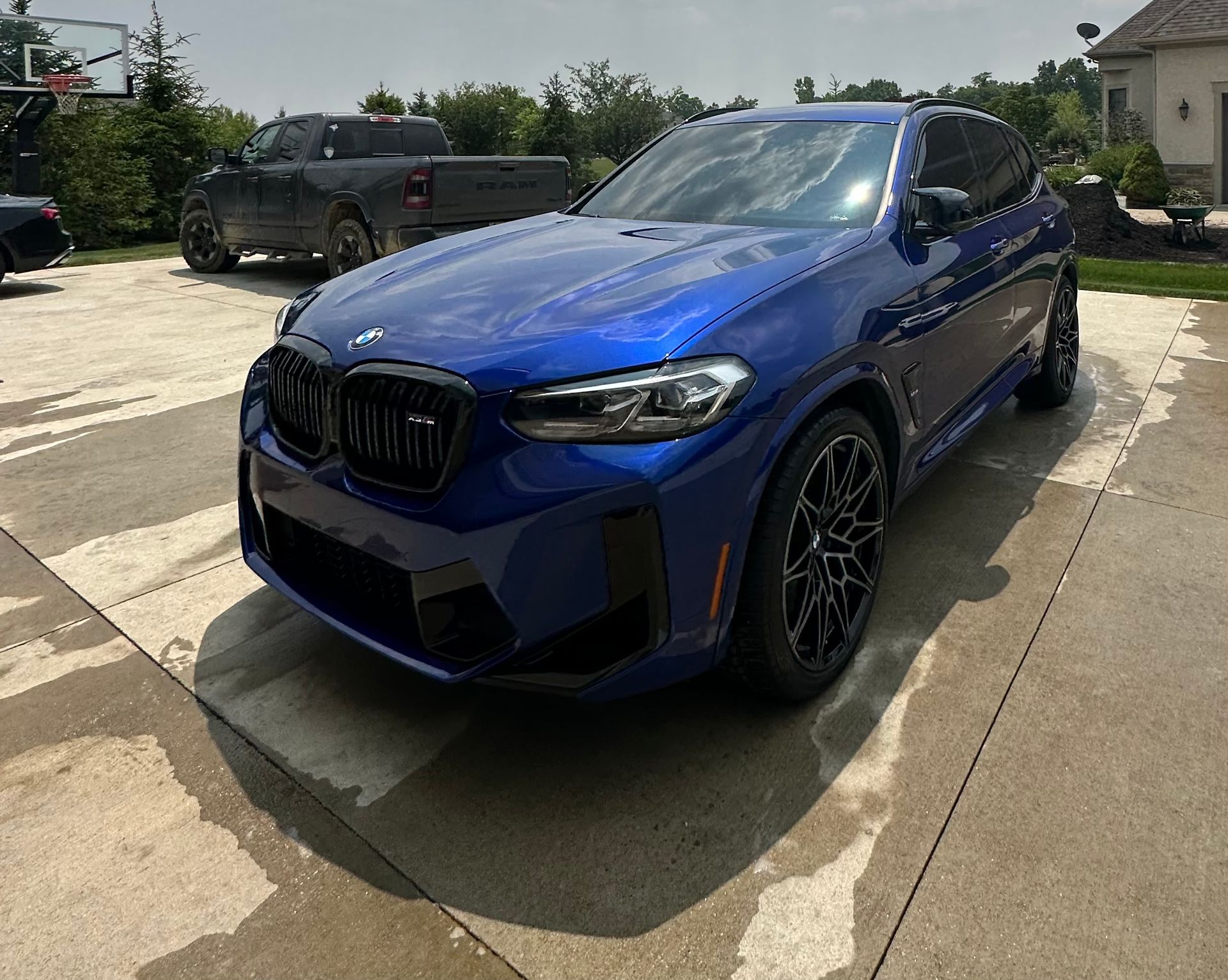 A blue bmw is parked in a driveway next to a truck.