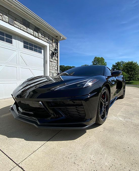 A black corvette is parked in front of a garage.