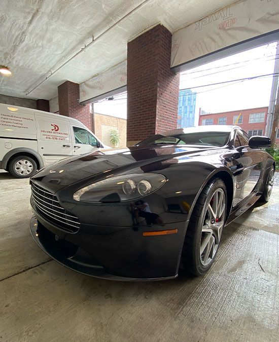 A black sports car is parked in a garage next to a white van.