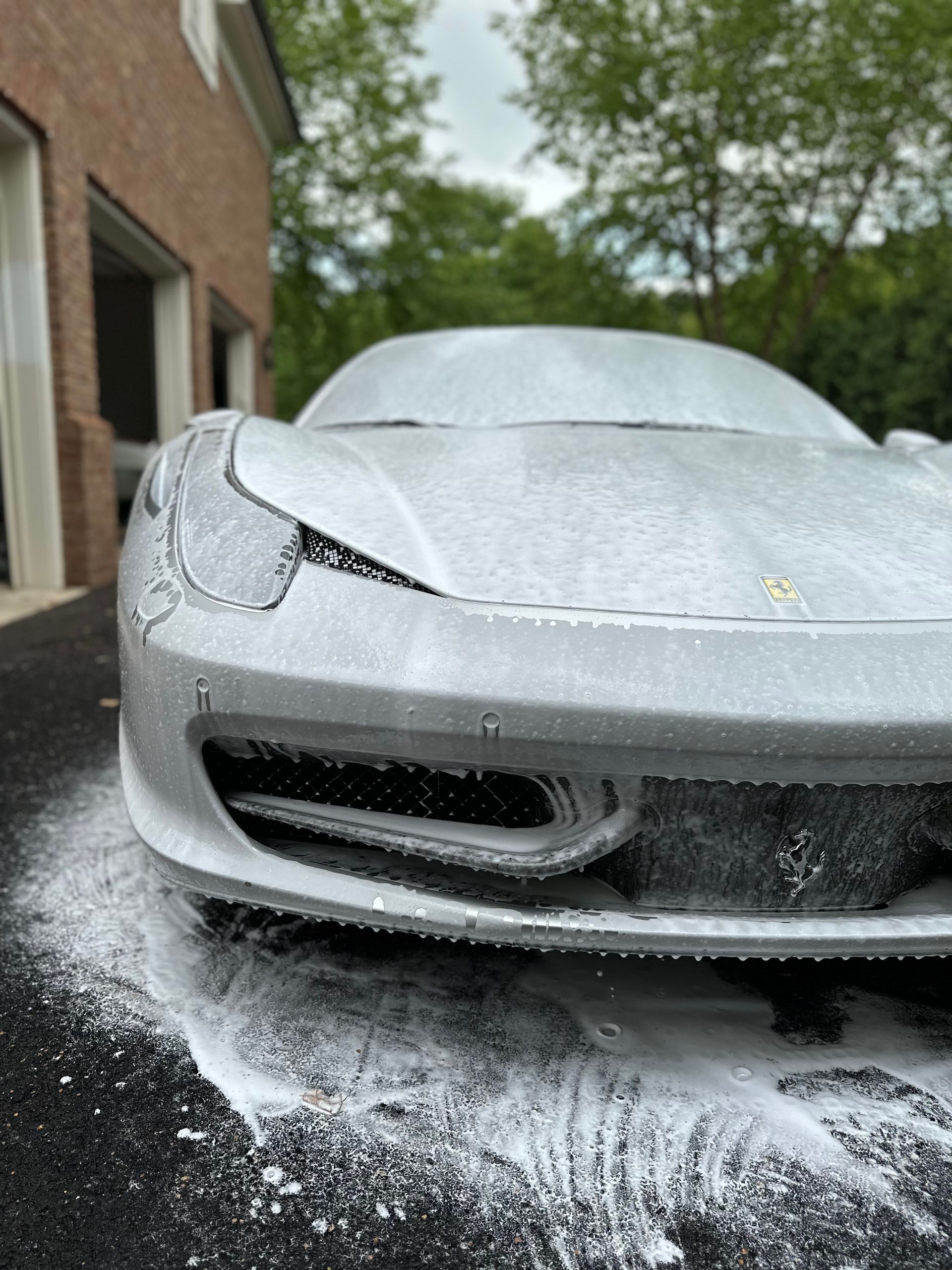 A silver sports car is covered in foam in a driveway.