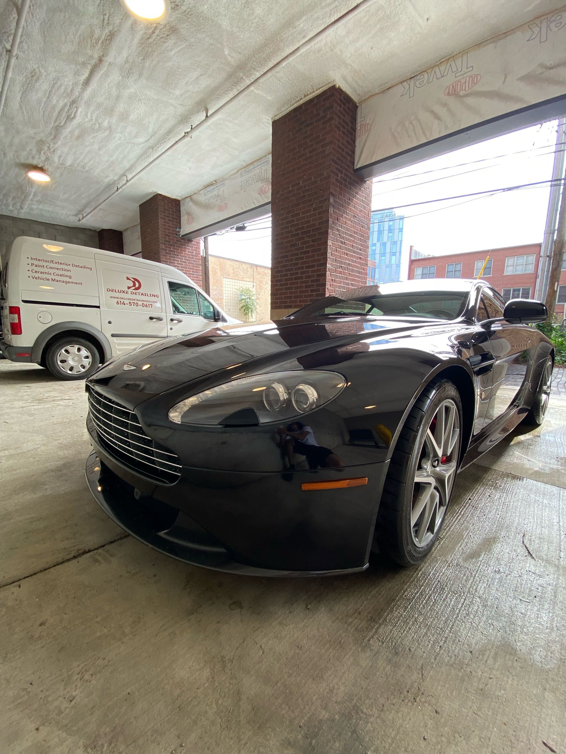 A black sports car is parked in a garage next to a white van.