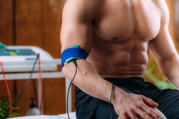 Un uomo a torso nudo è seduto su un letto con un dispositivo al braccio.