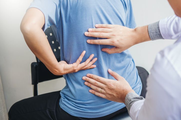 Un uomo è seduto su una sedia mentre un medico gli visita la schiena.