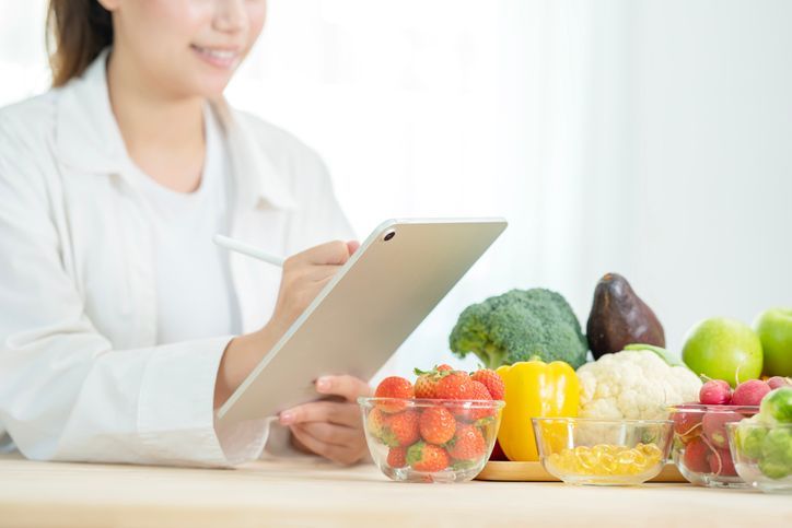 Una donna sta usando un tablet davanti a ciotole di frutta e verdura.