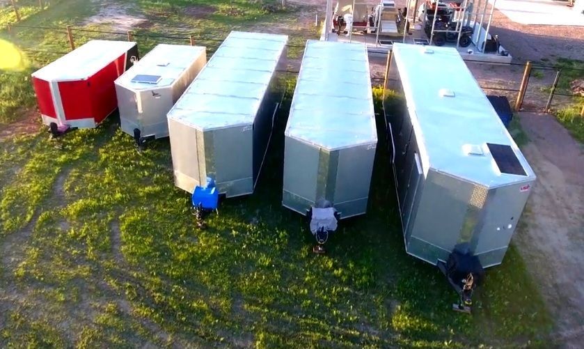Aerial view of several small metal trailers and a red utility trailer parked on grass.