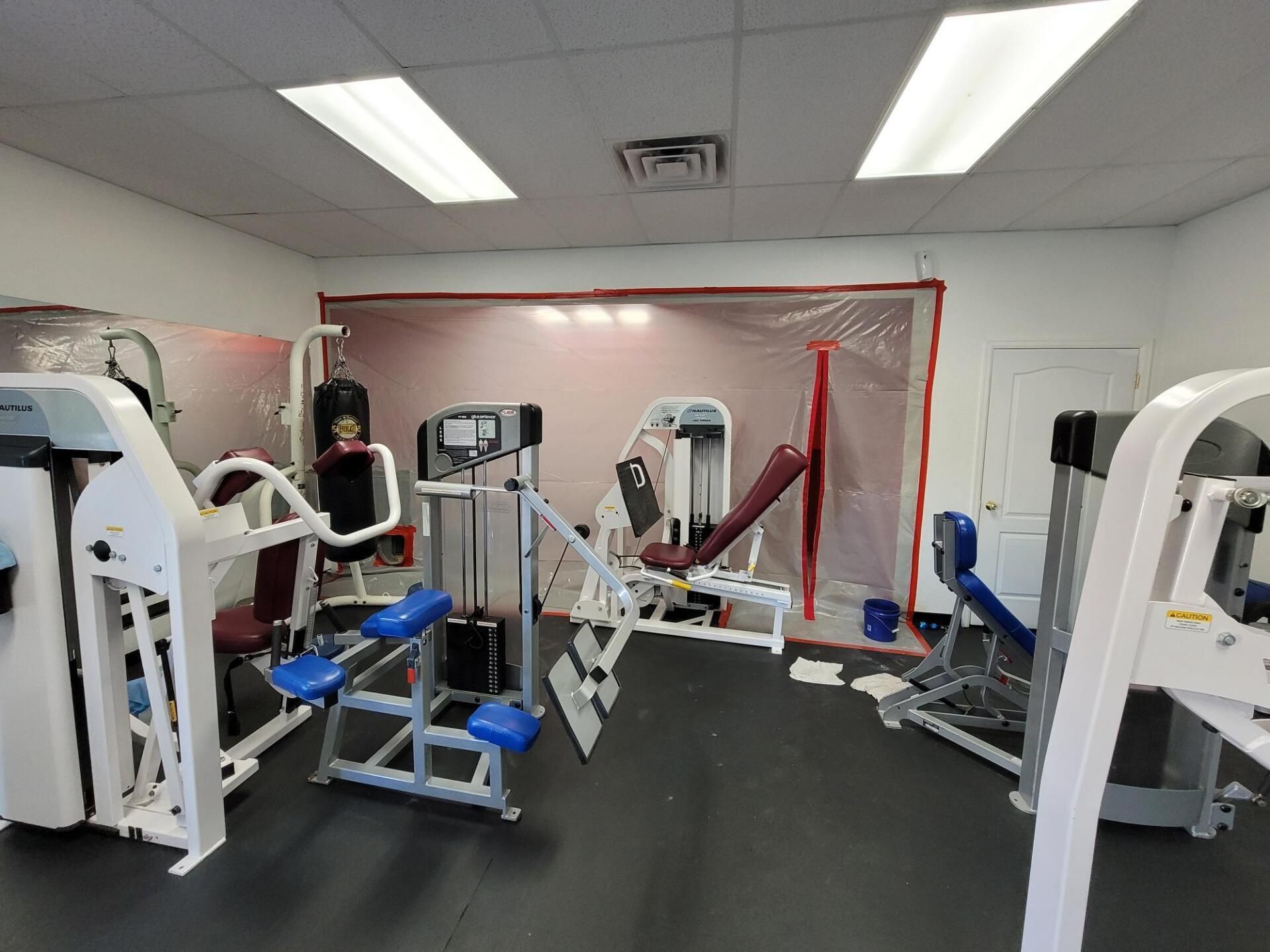Gym room with exercise machines, blue benches, and a gray floor under bright ceiling lights