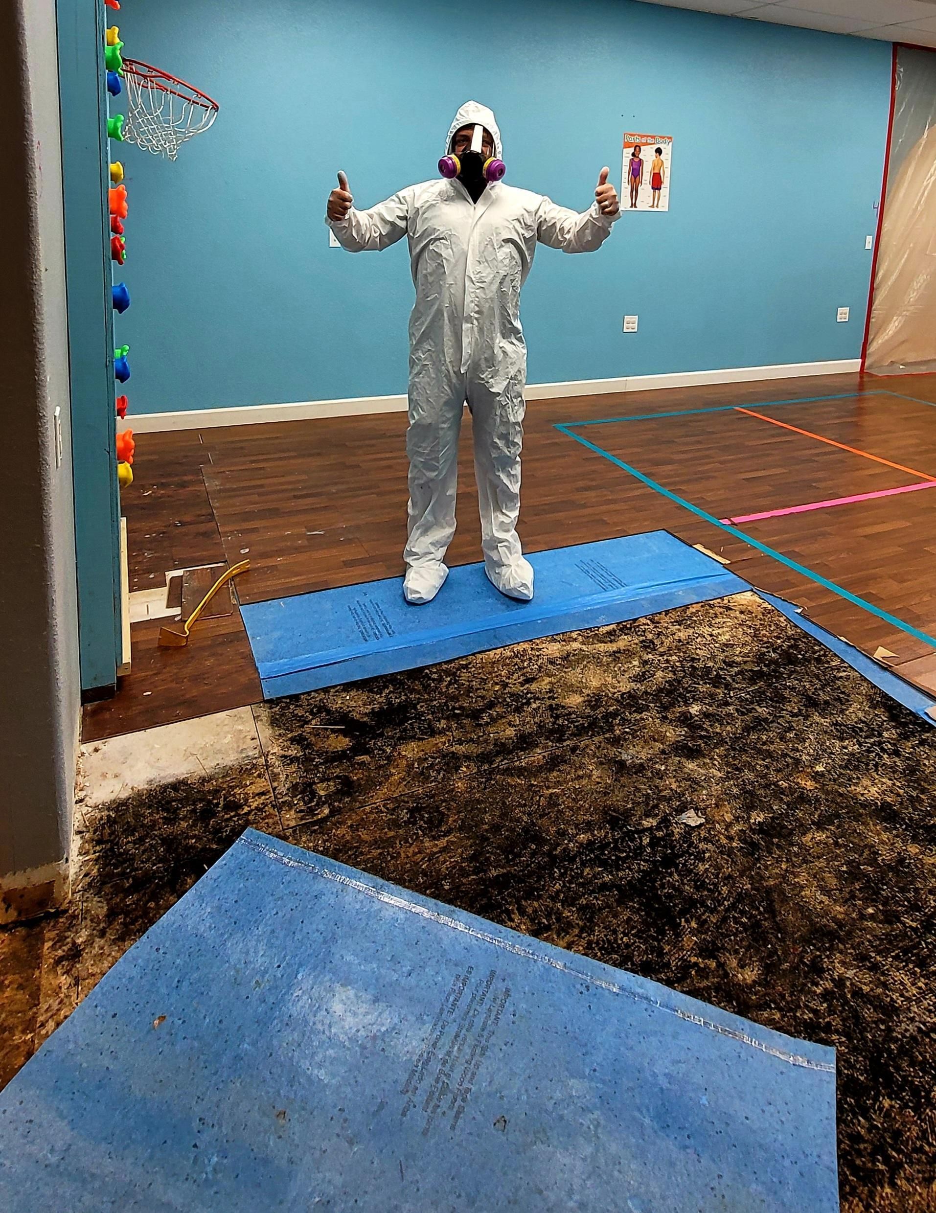 Person in a white suit and mask standing on a blue mat in a colorful indoor room with arms raised.