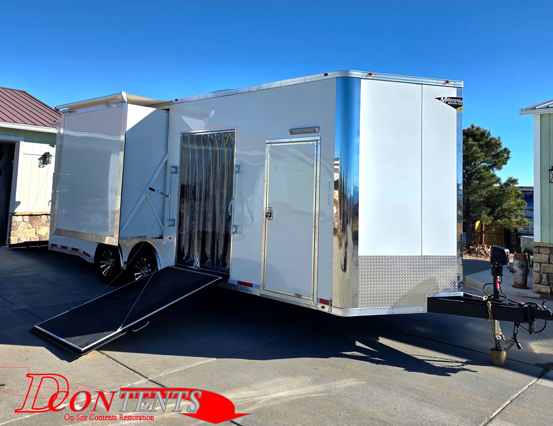 White enclosed utility trailer with open side ramp parked on a sunny street.