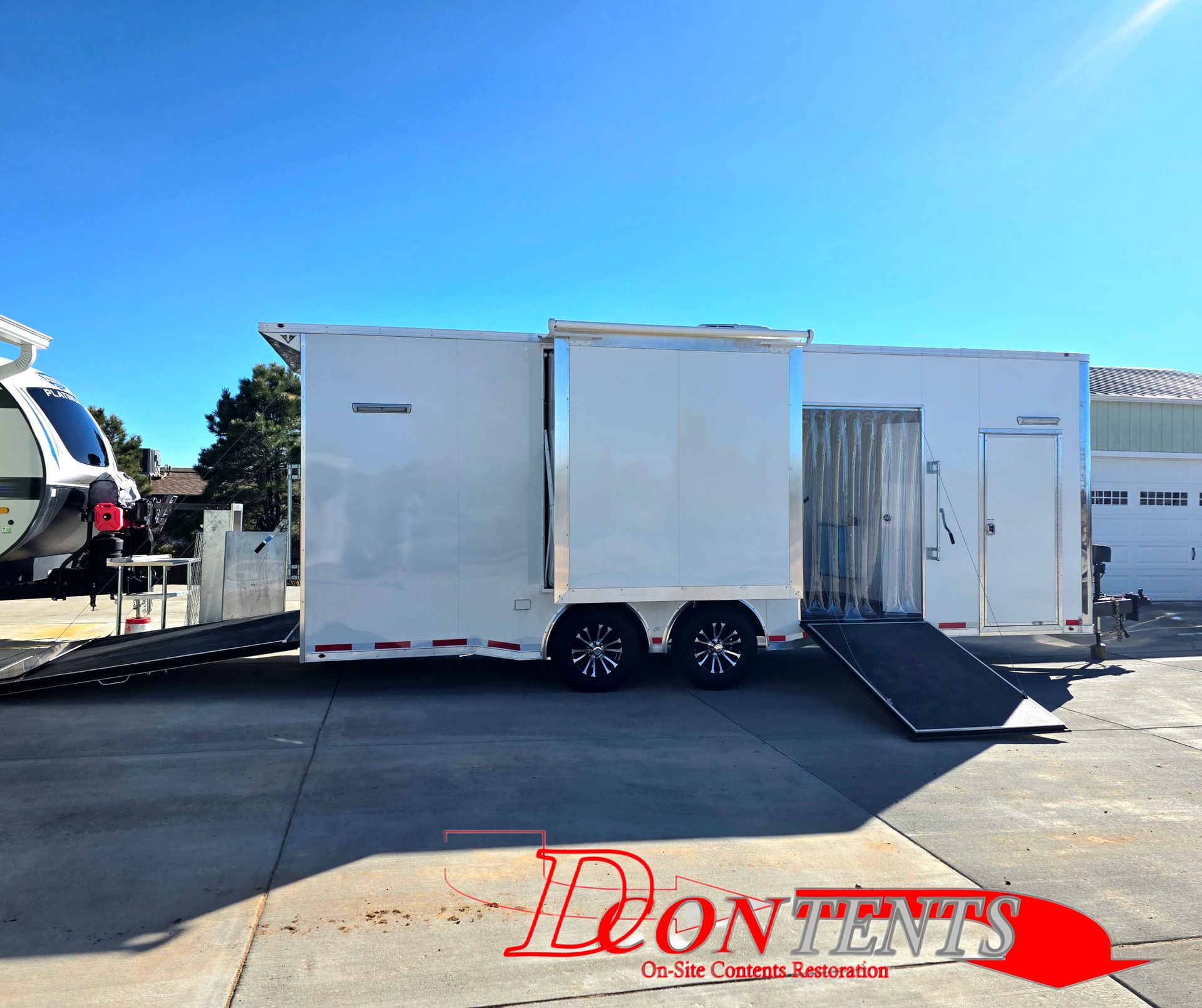 White enclosed trailer with a side ramp parked on a sunny lot under a blue sky.