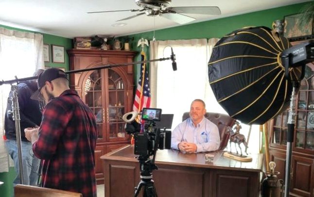 Photo studio with photographer, seated subject, and large umbrella light in a living room setting