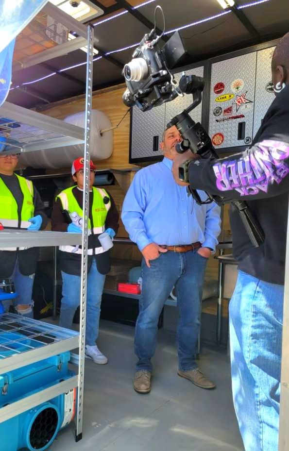 Camera crew filming a man in a blue shirt inside a workshop or garage.
