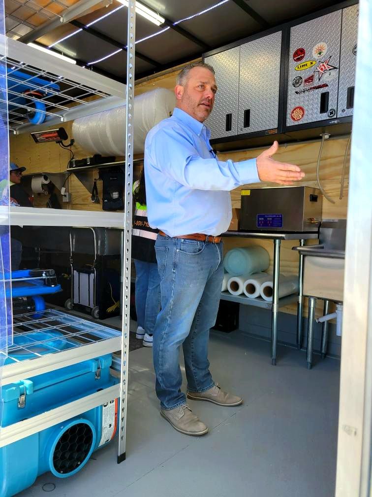 Man gesturing inside a van filled with shelving, tools, and equipment.