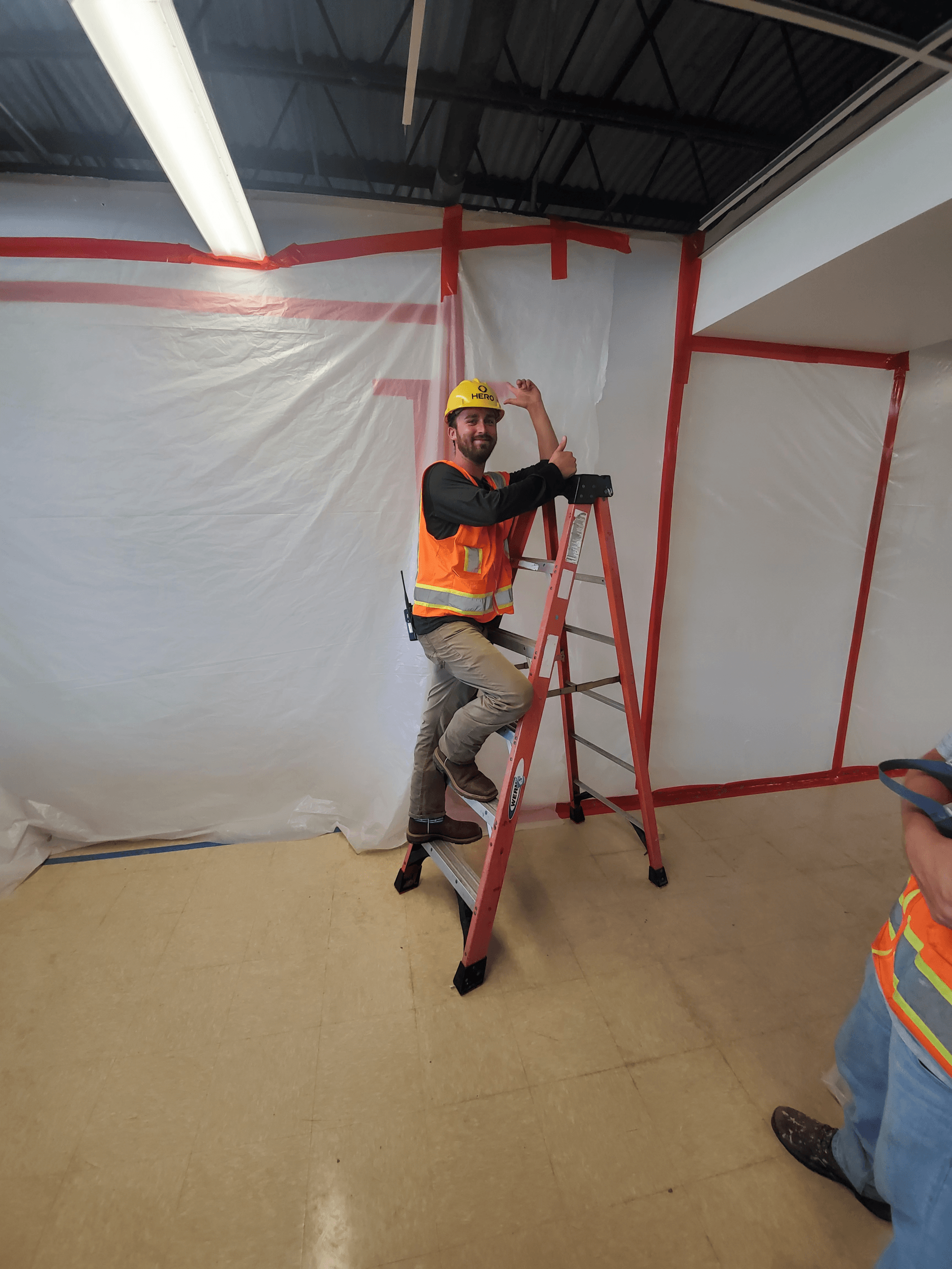 Worker in hard hat adjusting a ladder inside a taped-off construction area