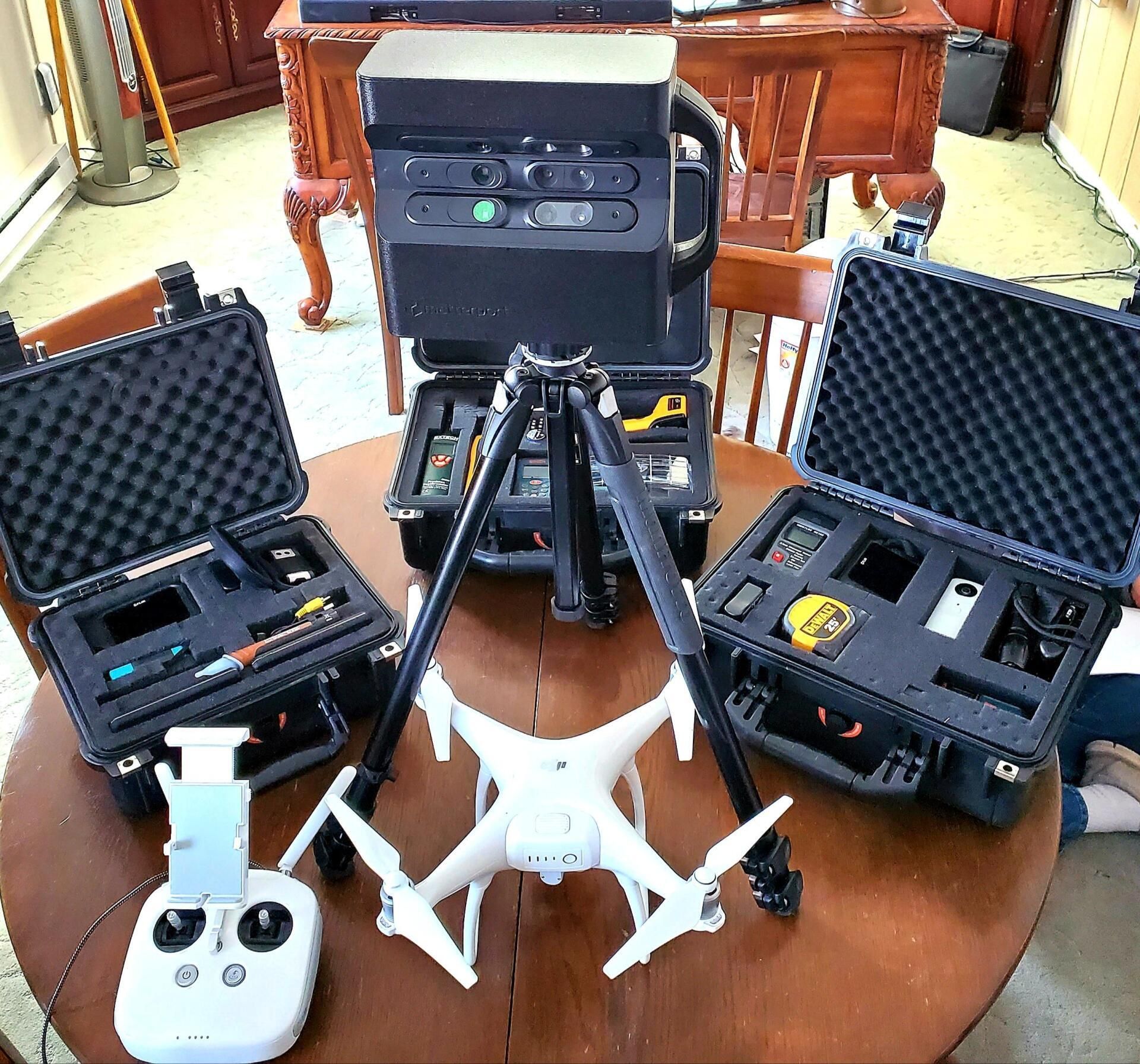 Two white drones, a controller, and open black equipment cases on a wooden table indoors.