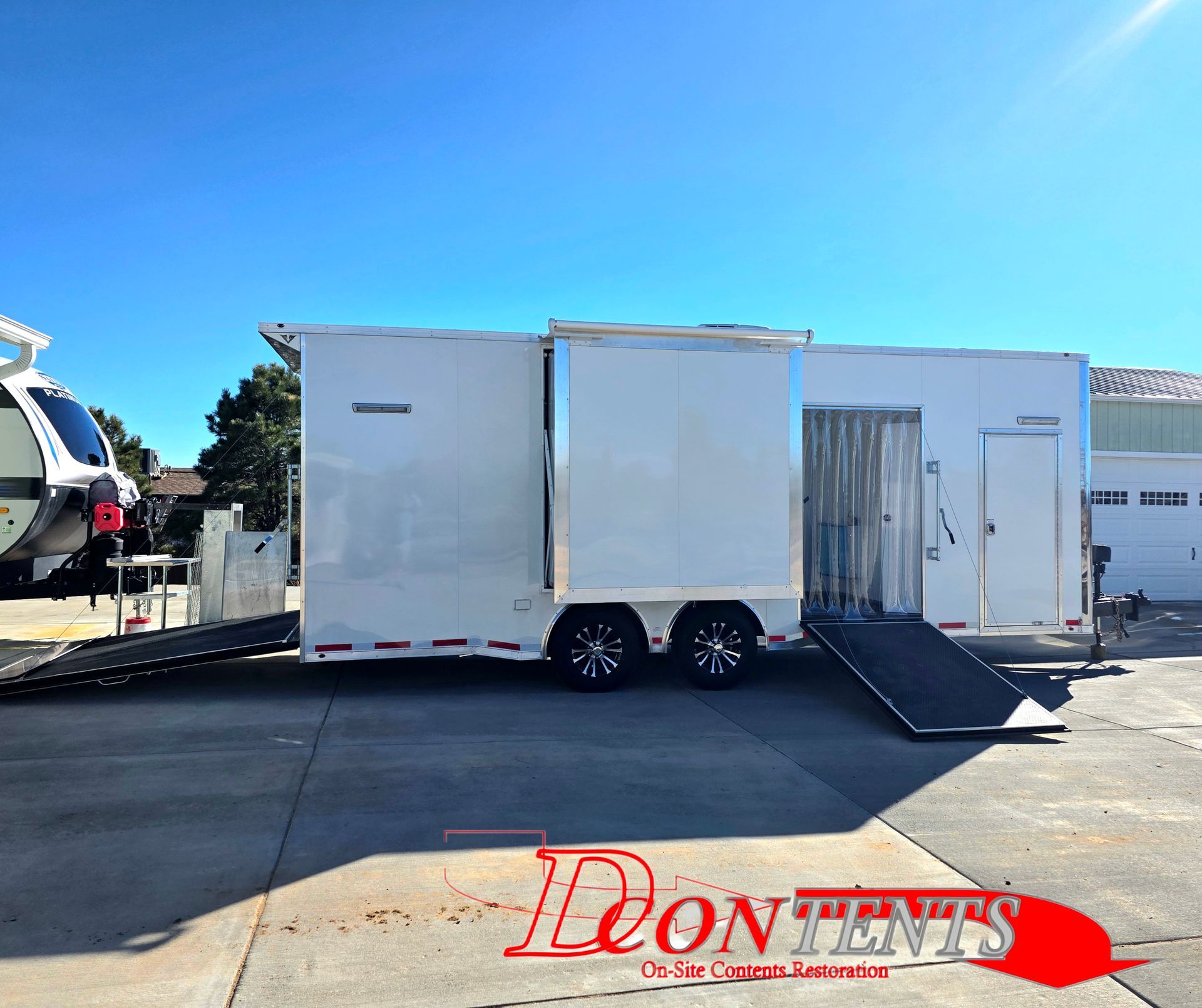 White enclosed trailer with a side ramp parked on a sunny lot under a blue sky.
