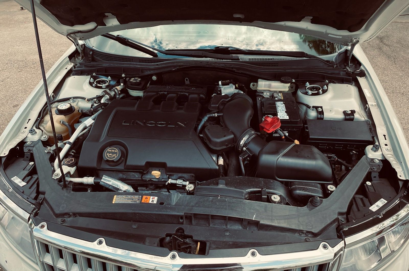 The engine of a silver car is shown with the hood open.