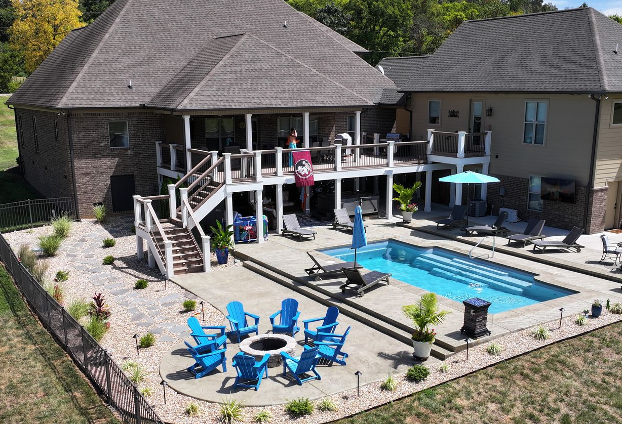 House with pool and deck, surrounded by landscaping, under a blue sky.