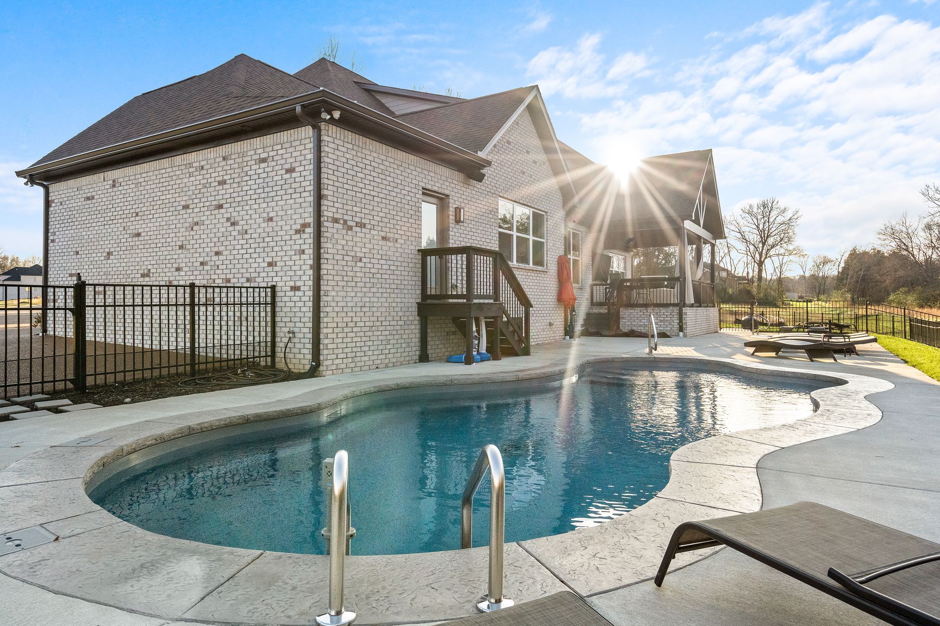 House exterior with a pool, brick walls, a wooden deck, and sunny blue sky.