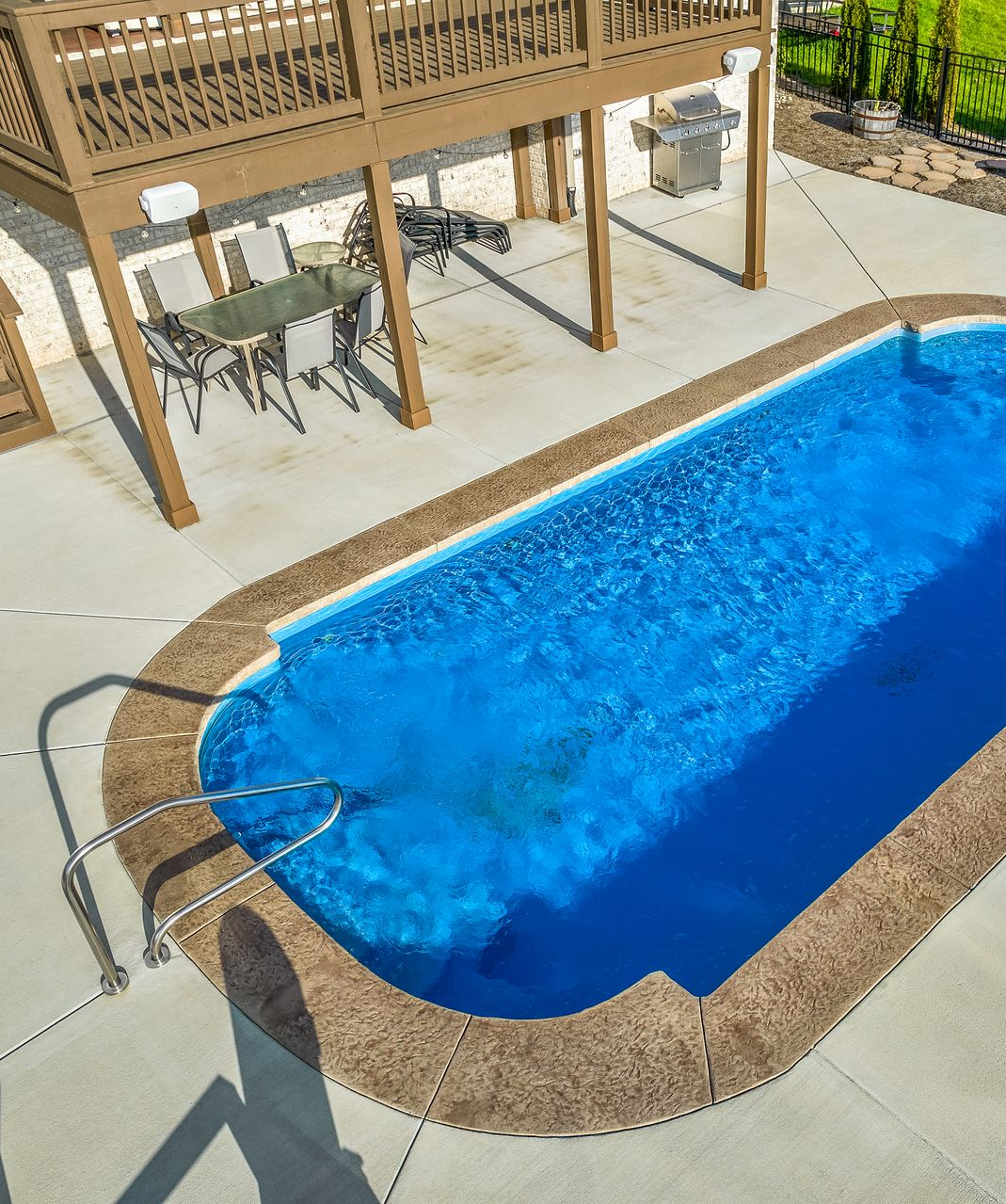 Swimming pool with blue water and patio furniture under a wooden pergola.