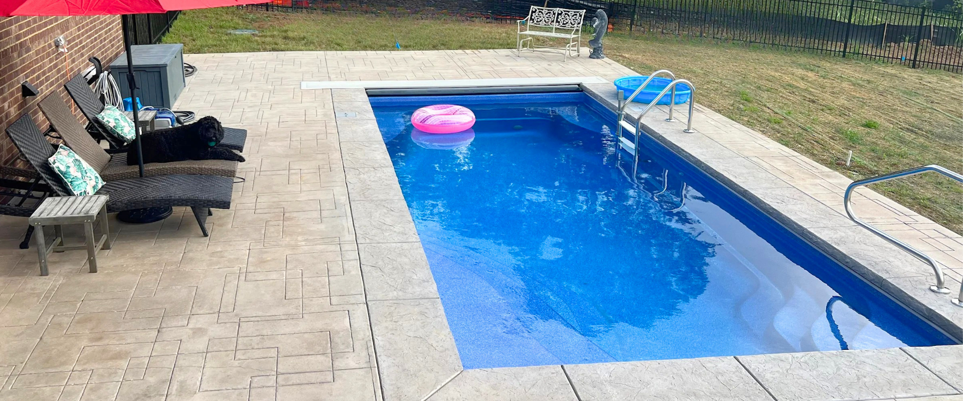 Backyard swimming pool with blue water, pink float, patio chairs, and stone paving