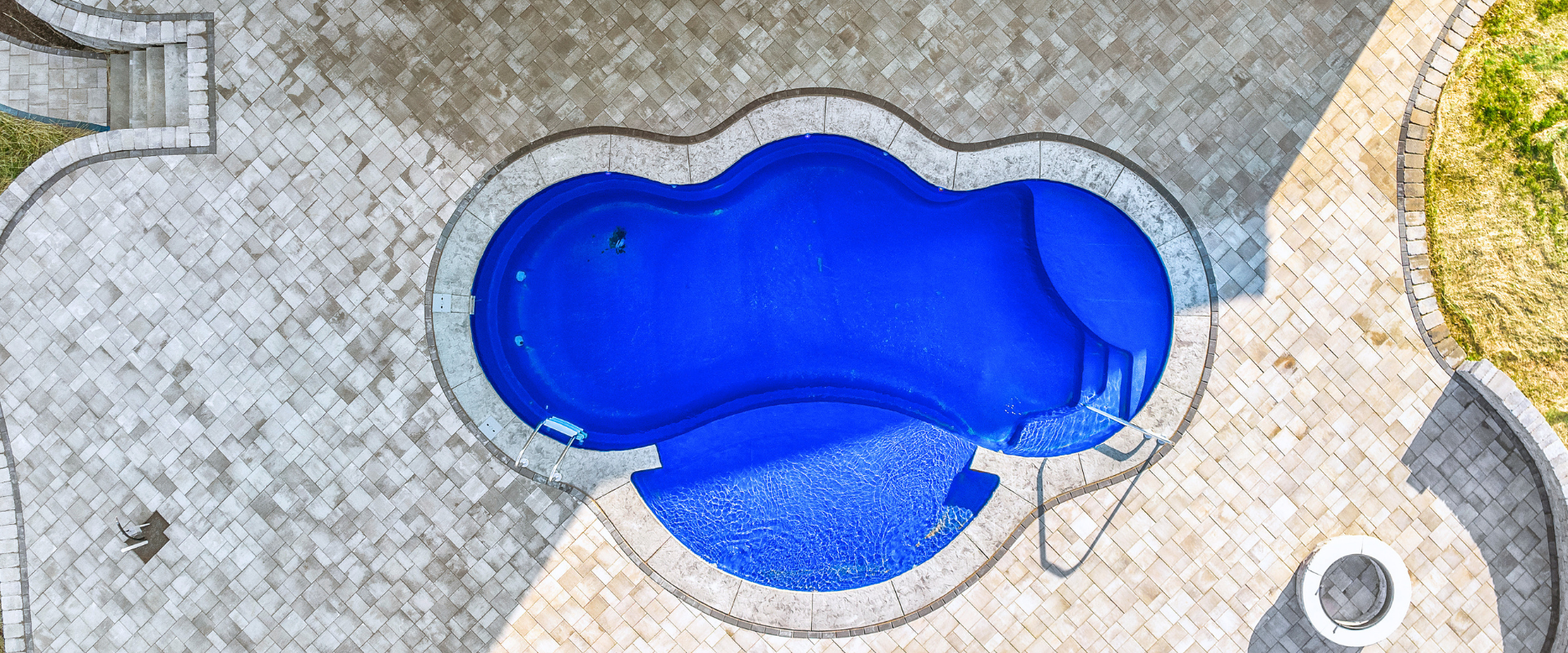 Overhead view of a blue swimming pool surrounded by stone patio and paving stones